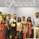 Premio ADUT 2019 grupo de personas posando juntas en el interior de una habitación o negocio con un letrero de neón que dice "Gracias" arriba a la izquierda.