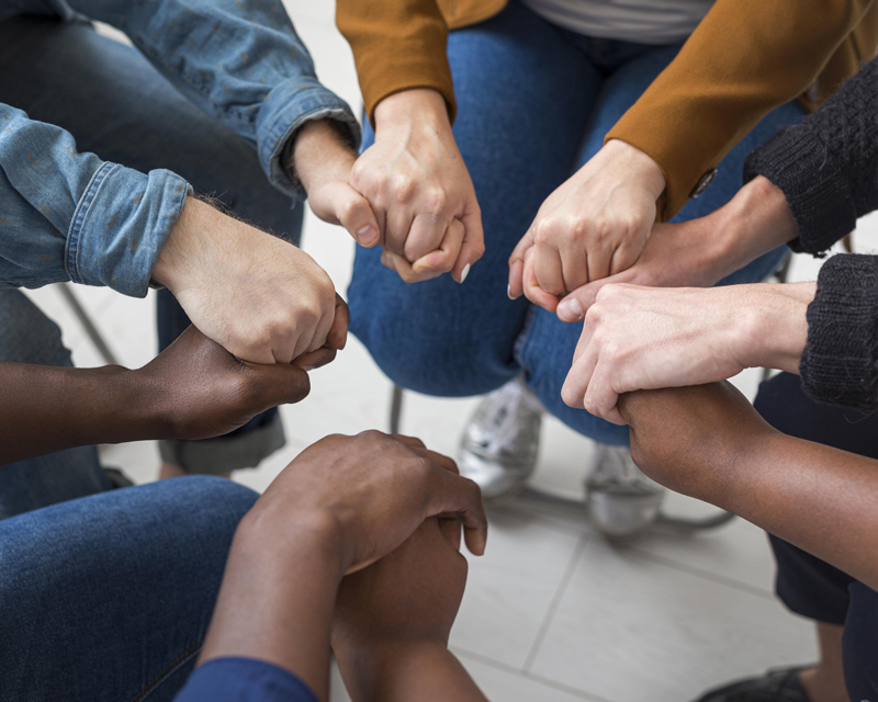 objetivos un grupo de personas sentadas en círculo y cogidas de la mano, lo cual simboliza unidad, apoyo, solidaridad y trabajo en equipo